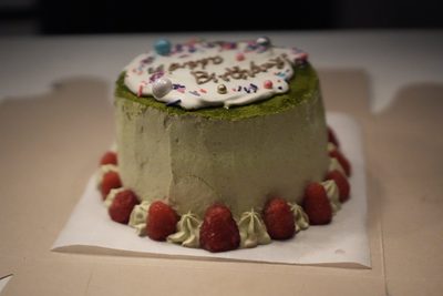 A matcha birthday cake ringed with raspberries and piped cream, with Happy Birthday written across a white disc on top