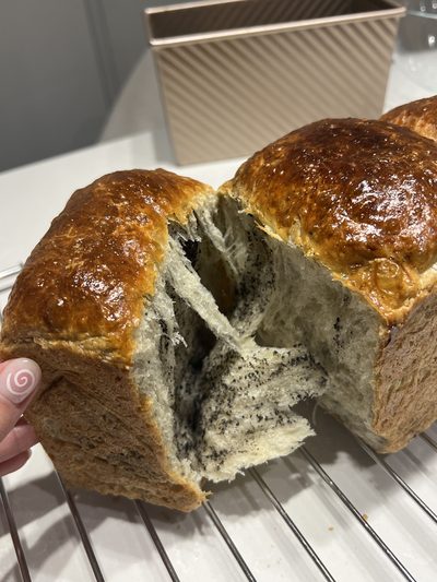 A loaf of black sesame swirl milk bread torn open by hand to show the marbled, feathery crumb inside