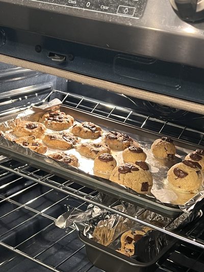 Chocolate chunk cookies spread across a foil-lined tray inside a hot oven