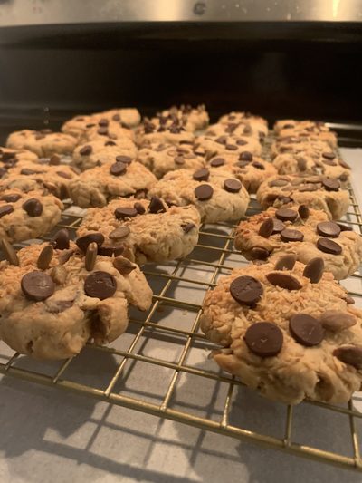 Coconut chocolate chip cookies studded with chocolate buttons, cooling on a wire rack