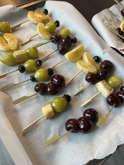 Wooden skewers of candied fruit — green grapes, mandarin segments, cherries and blueberries — glossy with a hardened sugar shell
