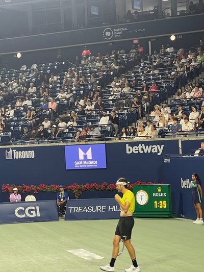 A player in a yellow shirt walking the baseline between points on a stadium court, the match clock reading one thirty-five