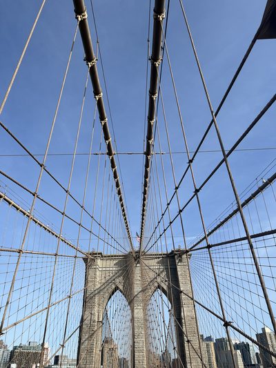 The stone tower and fanned steel cables of the Brooklyn Bridge photographed from the walkway against a clear blue sky