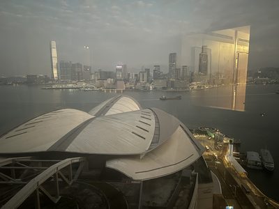 Hong Kong harbour at dusk seen from above, the convention centre's curved white roof in the foreground and the Kowloon skyline lit across the water