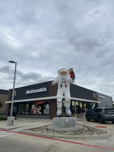 A life-size astronaut statue holding up a carton of fries outside a McDonald's near Houston, under a heavy grey sky